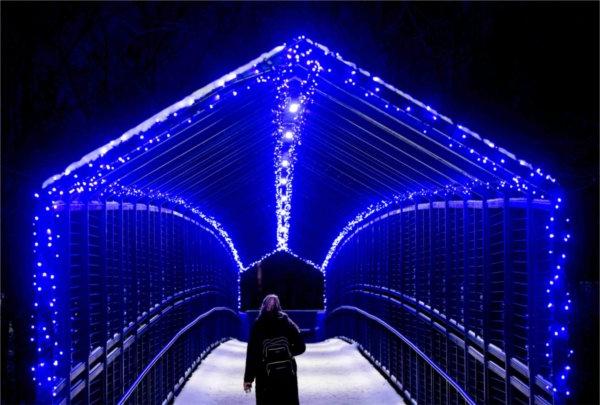  A student wearing a backpack walks over a blue-lit bridge. 