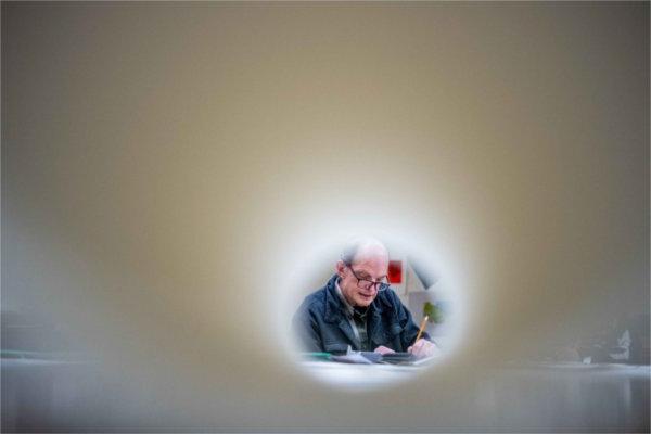  A professor with glasses resting on his nose and holding a pencil talks to students as seen through a roll of paper. 